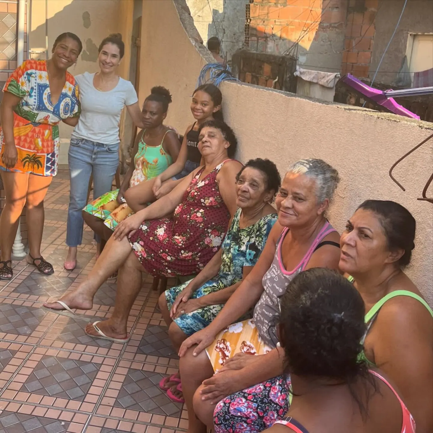 Juliana Benício sentada entre moradoras e crianças em atividade na comunidade